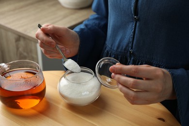 Photo of Woman adding sugar into aromatic tea at wooden table indoors, closeup