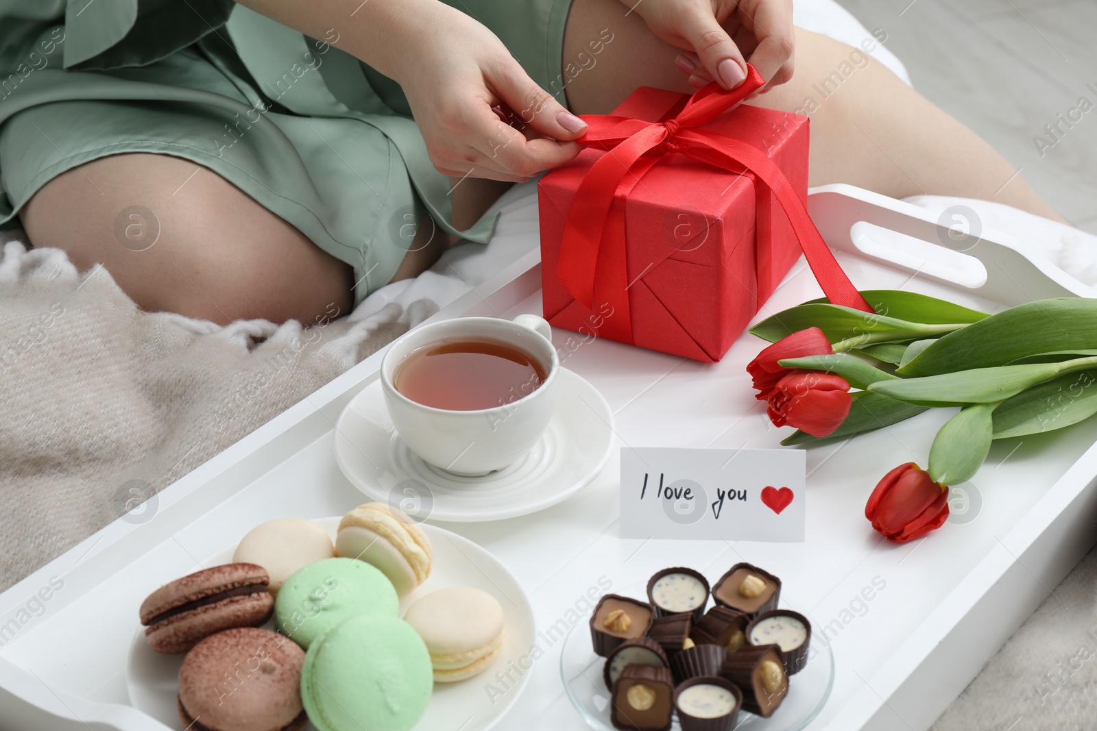 Photo of Tasty breakfast served in bed. Woman with gift box, desserts, tea, flowers and I Love You card at home, closeup