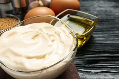 Photo of Glass bowl with fresh mayonnaise on black wooden table, closeup. Space for text