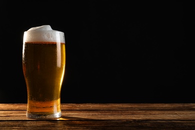 Photo of Cold tasty beer on wooden table against dark background. Space for text