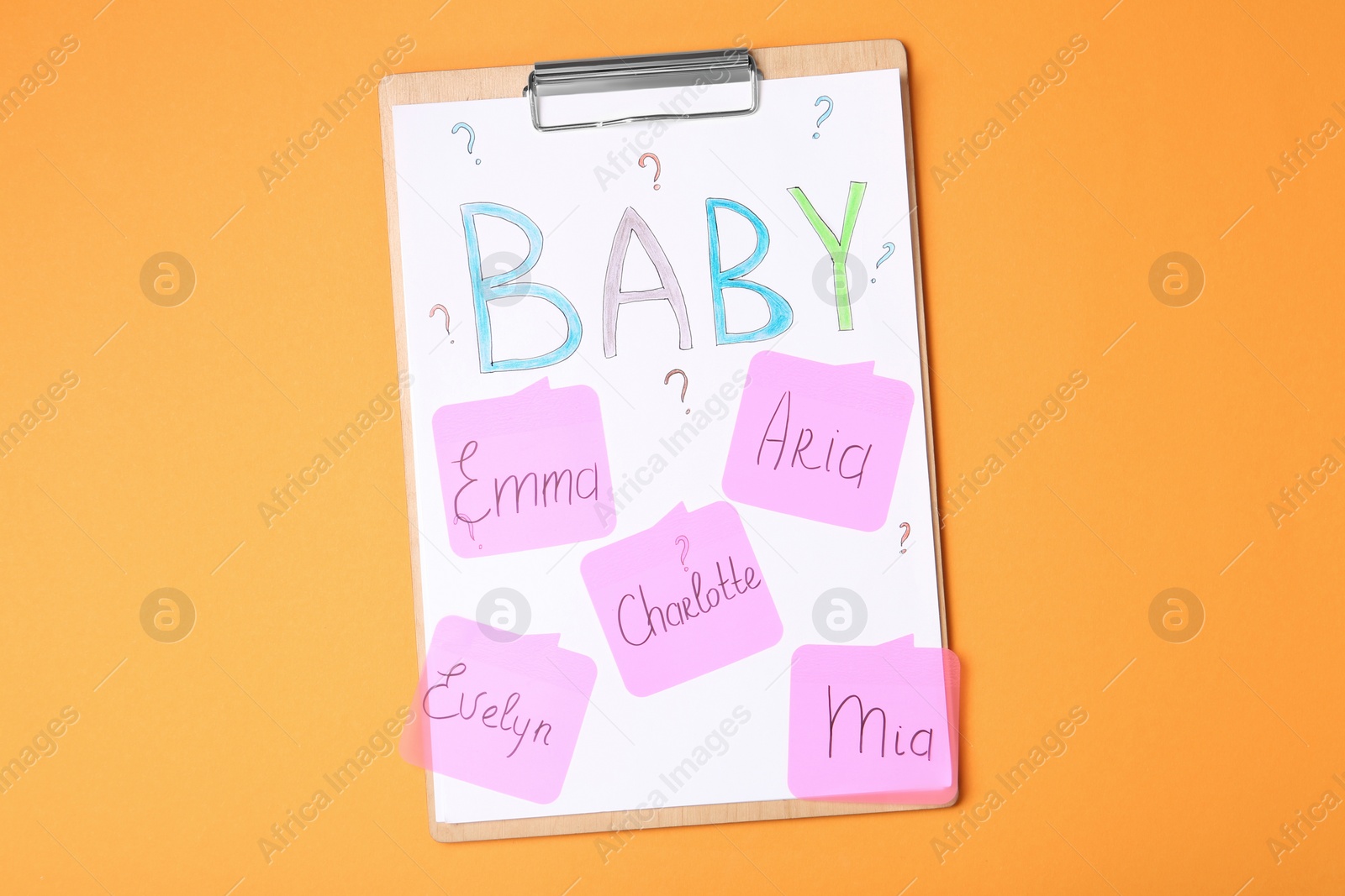 Photo of Clipboard with different baby names on orange background, top view