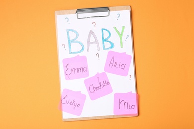 Photo of Clipboard with different baby names on orange background, top view