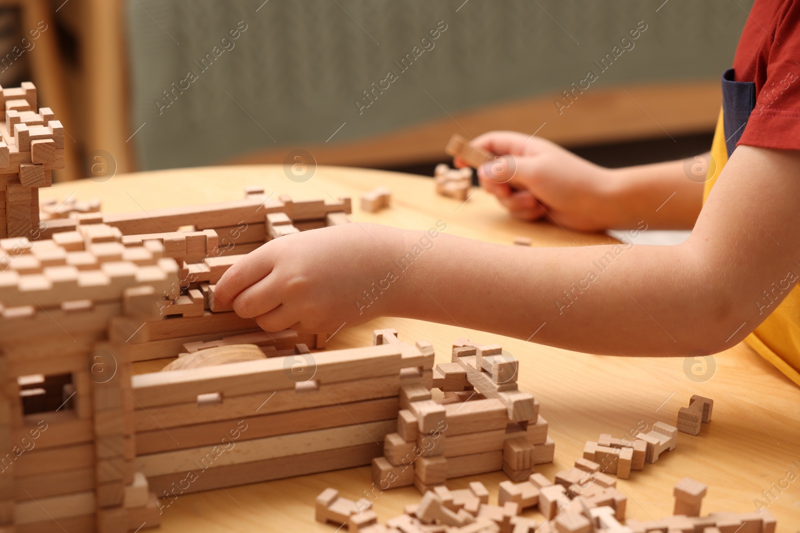 Photo of Little boy playing with wooden construction set at table indoors, closeup. Child's toy