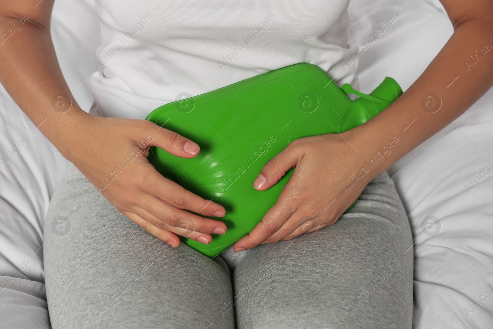 Photo of Young woman using hot water bottle to relieve cystitis pain on bed, closeup