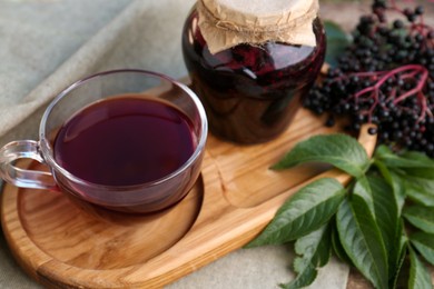 Elderberry jam, glass cup of tea and Sambucus berries on table