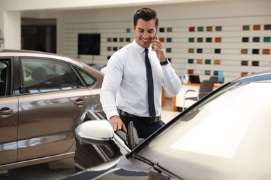 Photo of Young man talking on phone near car in modern dealership