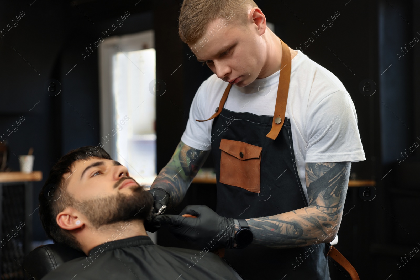 Photo of Professional hairdresser working with bearded client in barbershop