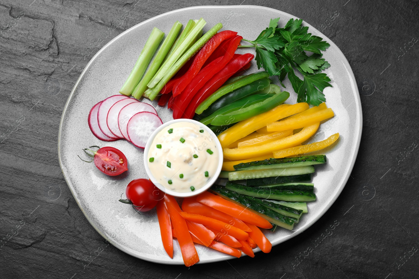 Photo of Fresh raw vegetable sticks and sauce on black table, top view