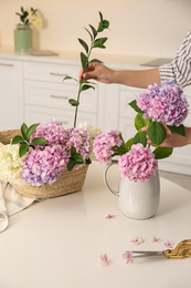 Photo of Woman making bouquet with beautiful hydrangea flowers at table indoors, closeup. Interior design element