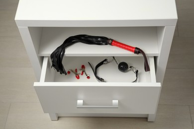 Photo of Black ball gag, whip and nipple clamps in drawer indoors, above view. Sex toys