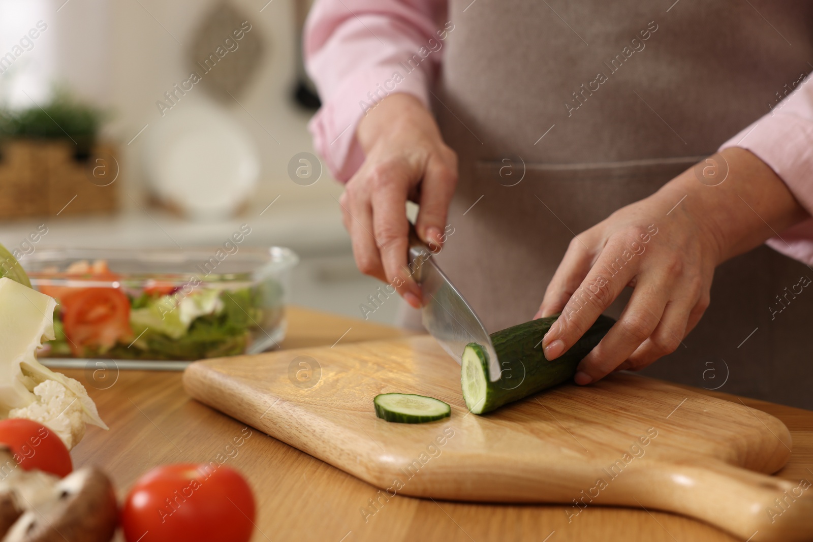 Photo of Woman cutting cucumber at wooden table in kitchen, closeup