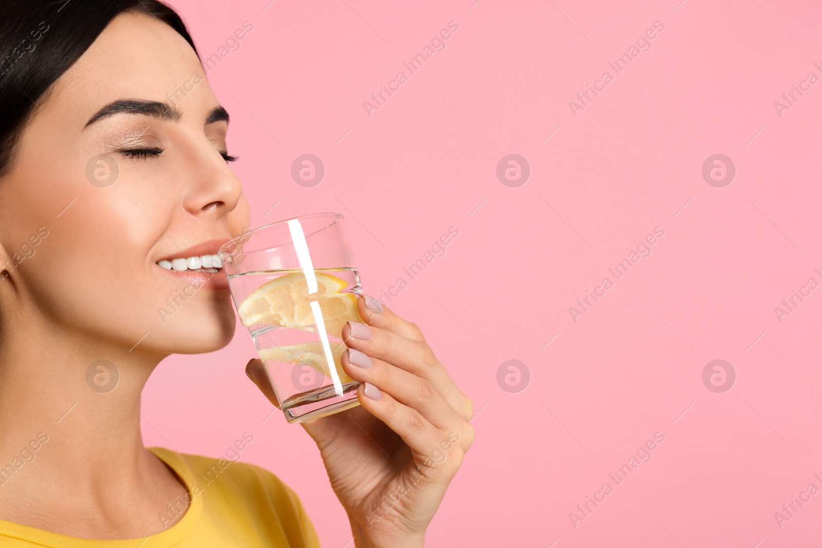 Photo of Beautiful young woman drinking tasty lemon water on pink background, closeup. Space for text