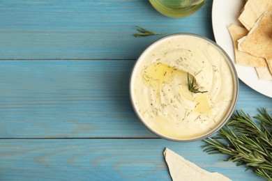 Photo of Delicious hummus with rosemary and pita chips on turquoise wooden table, flat lay. Space for text