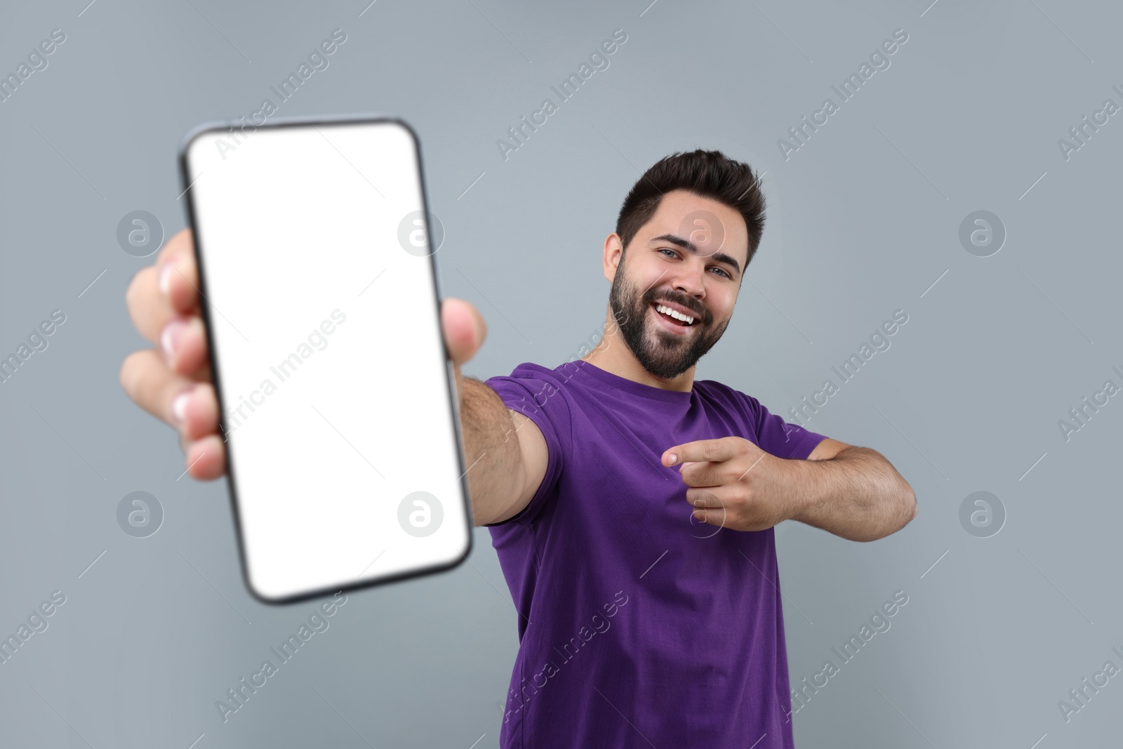 Photo of Young man showing smartphone in hand and pointing at it on light grey background