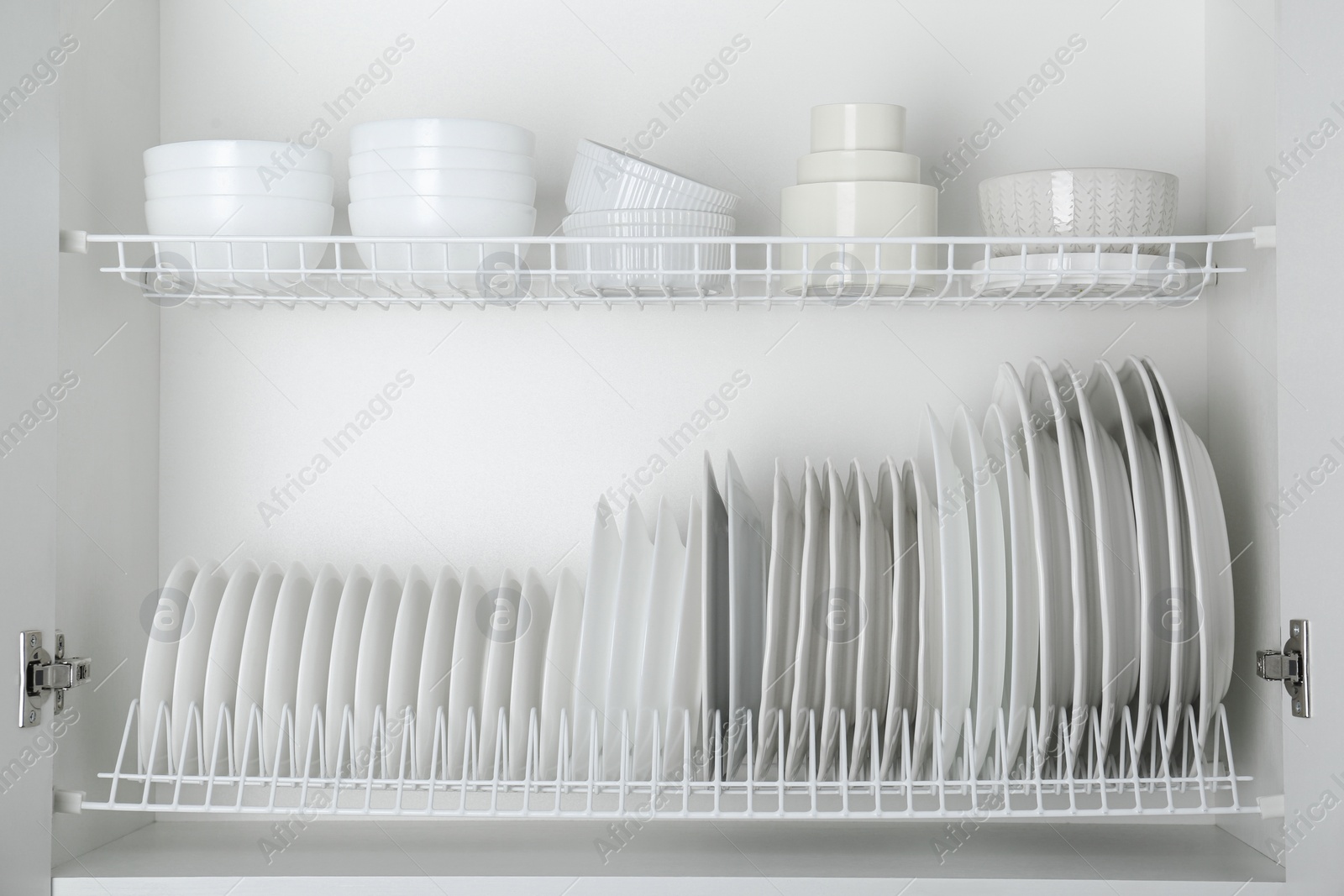 Photo of Different clean plates and bowls on shelves in cabinet