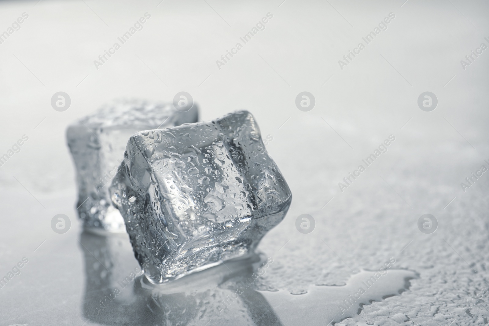 Photo of Crystal clear ice cubes with water drops on grey table, closeup. Space for text