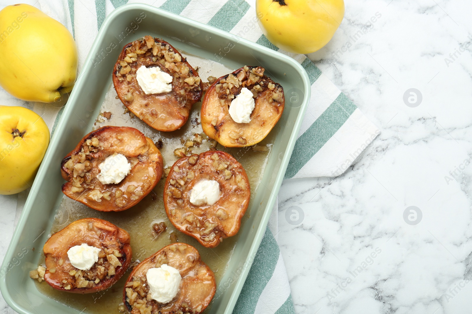 Photo of Tasty baked quinces with nuts and cream cheese in dish on white marble table, flat lay. Space for text