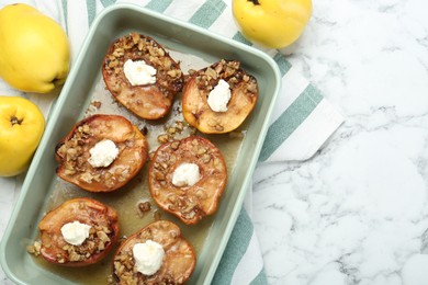 Photo of Tasty baked quinces with nuts and cream cheese in dish on white marble table, flat lay. Space for text