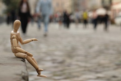 Photo of Wooden human figure sitting on curb outdoors, space for text
