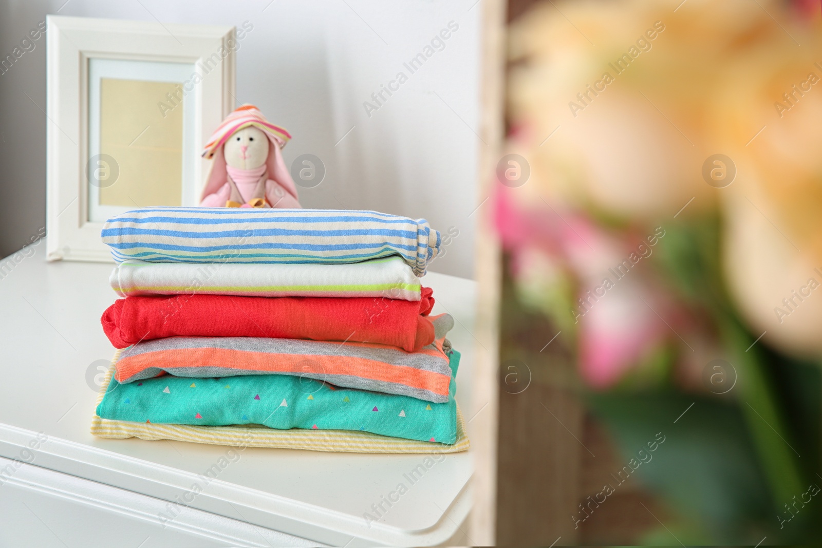 Photo of Toy bunny and stack of stylish child clothes on table indoors