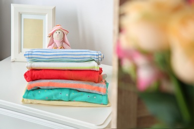 Toy bunny and stack of stylish child clothes on table indoors