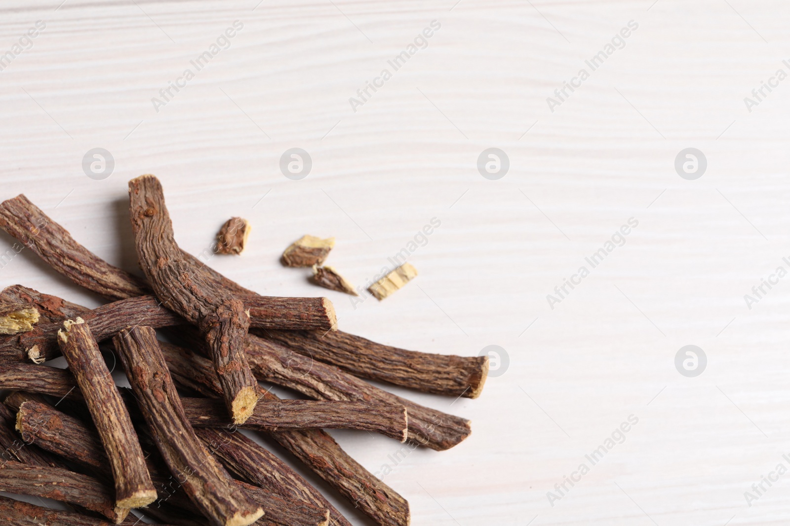 Photo of Dried sticks of liquorice root on white wooden table, space for text