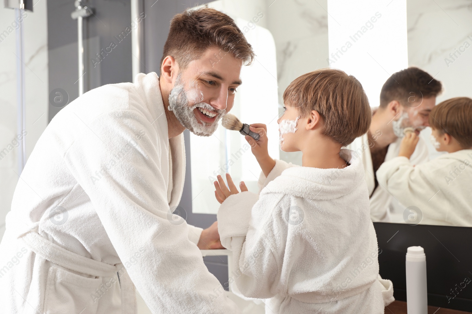 Photo of Dad and son with shaving foam on their faces having fun in bathroom