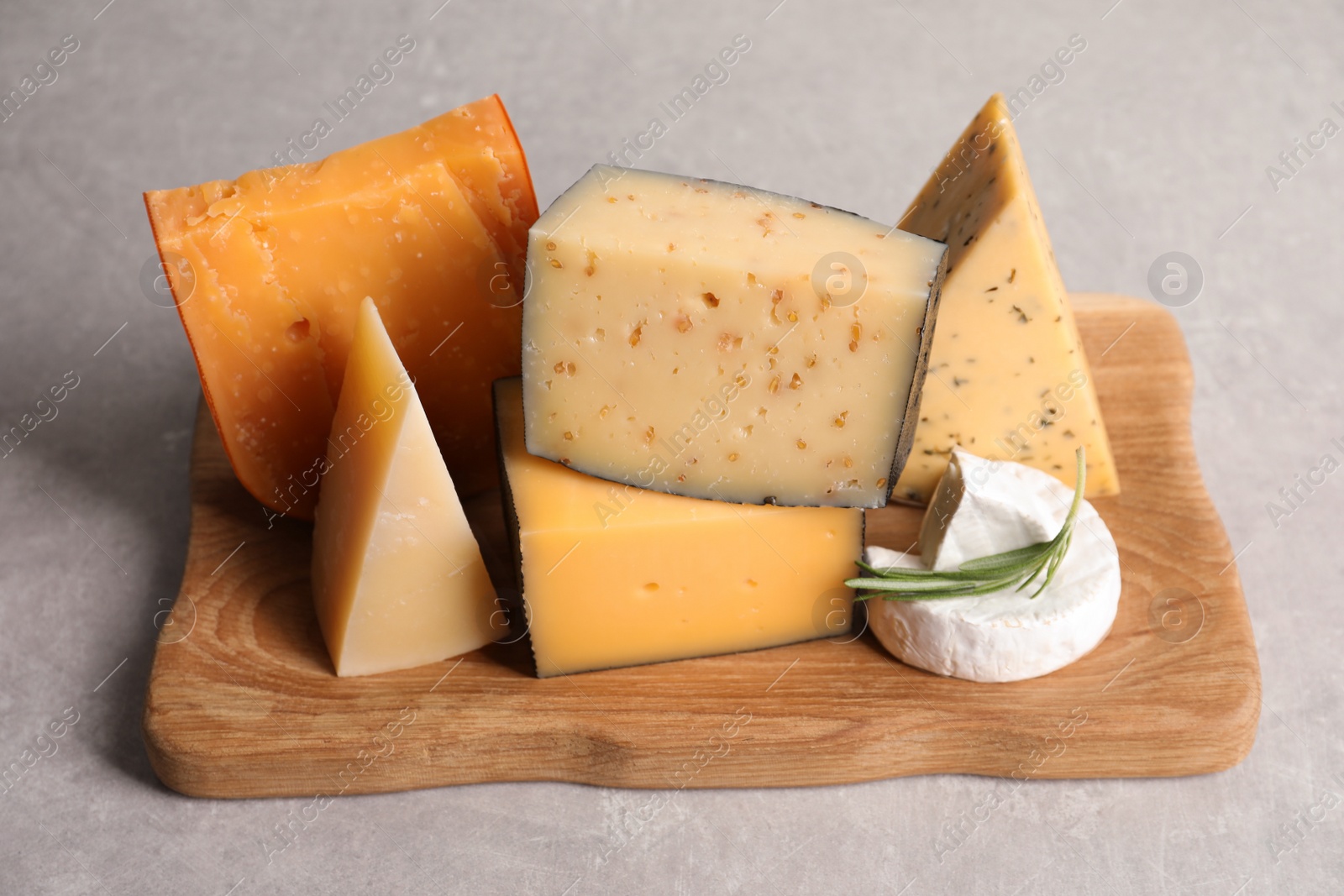 Photo of Wooden tray with different sorts of cheese and rosemary on grey table