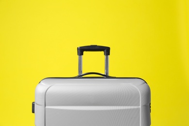 Stylish grey suitcase with handle on yellow background