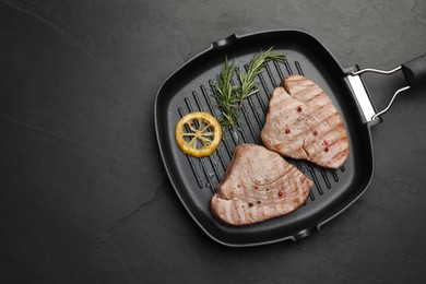 Photo of Delicious tuna steaks with lemon and rosemary on black table, top view. Space for text