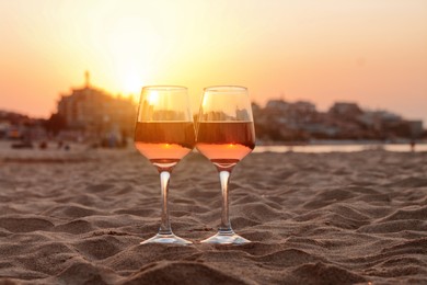 Glasses of tasty rose wine on sandy beach, space for text