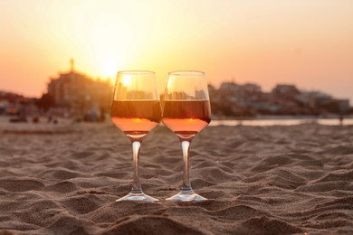 Photo of Glasses of tasty rose wine on sandy beach, space for text