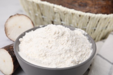 Photo of Bowl with cassava flour and roots on table, closeup