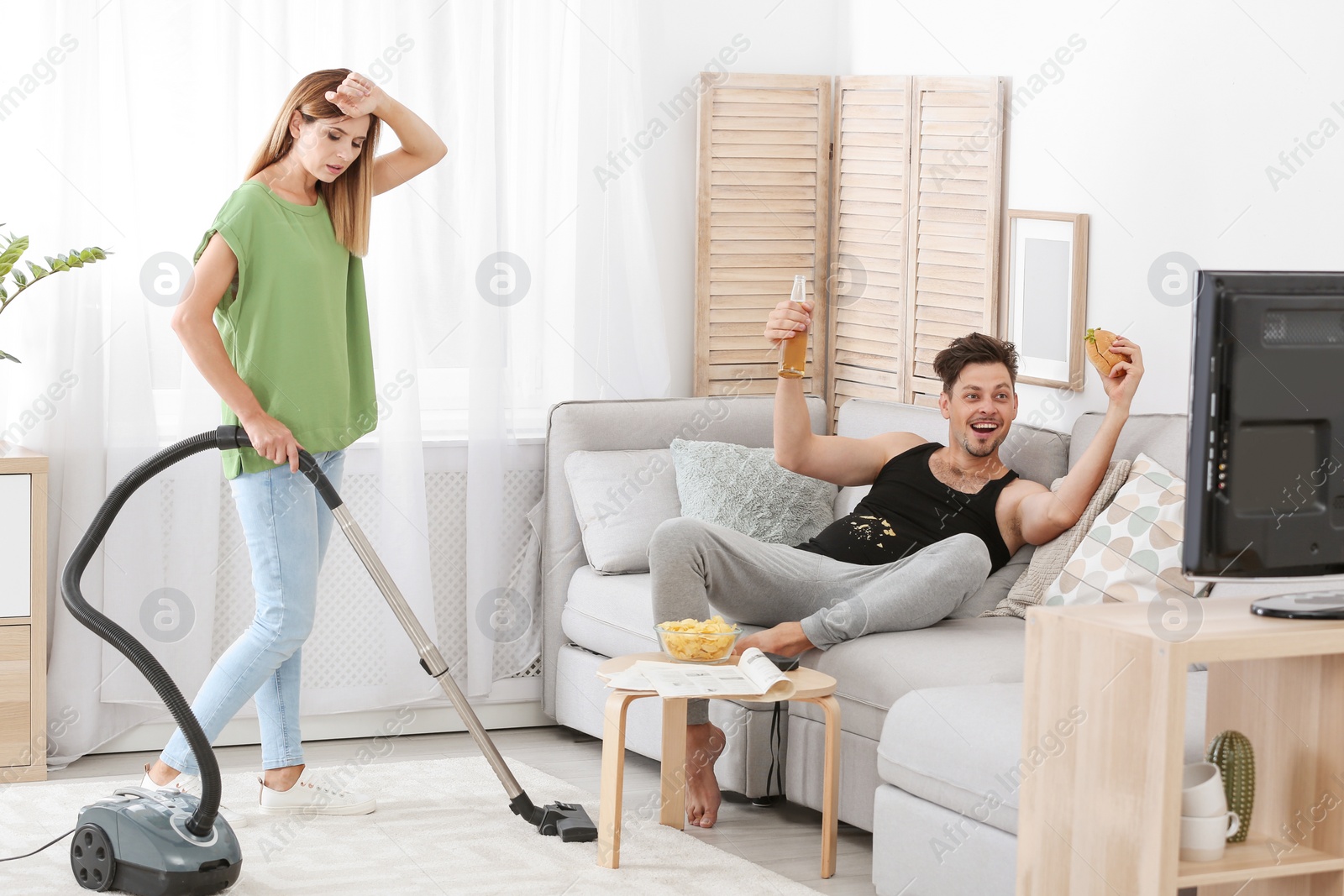 Photo of Lazy husband watching TV and his wife cleaning at home