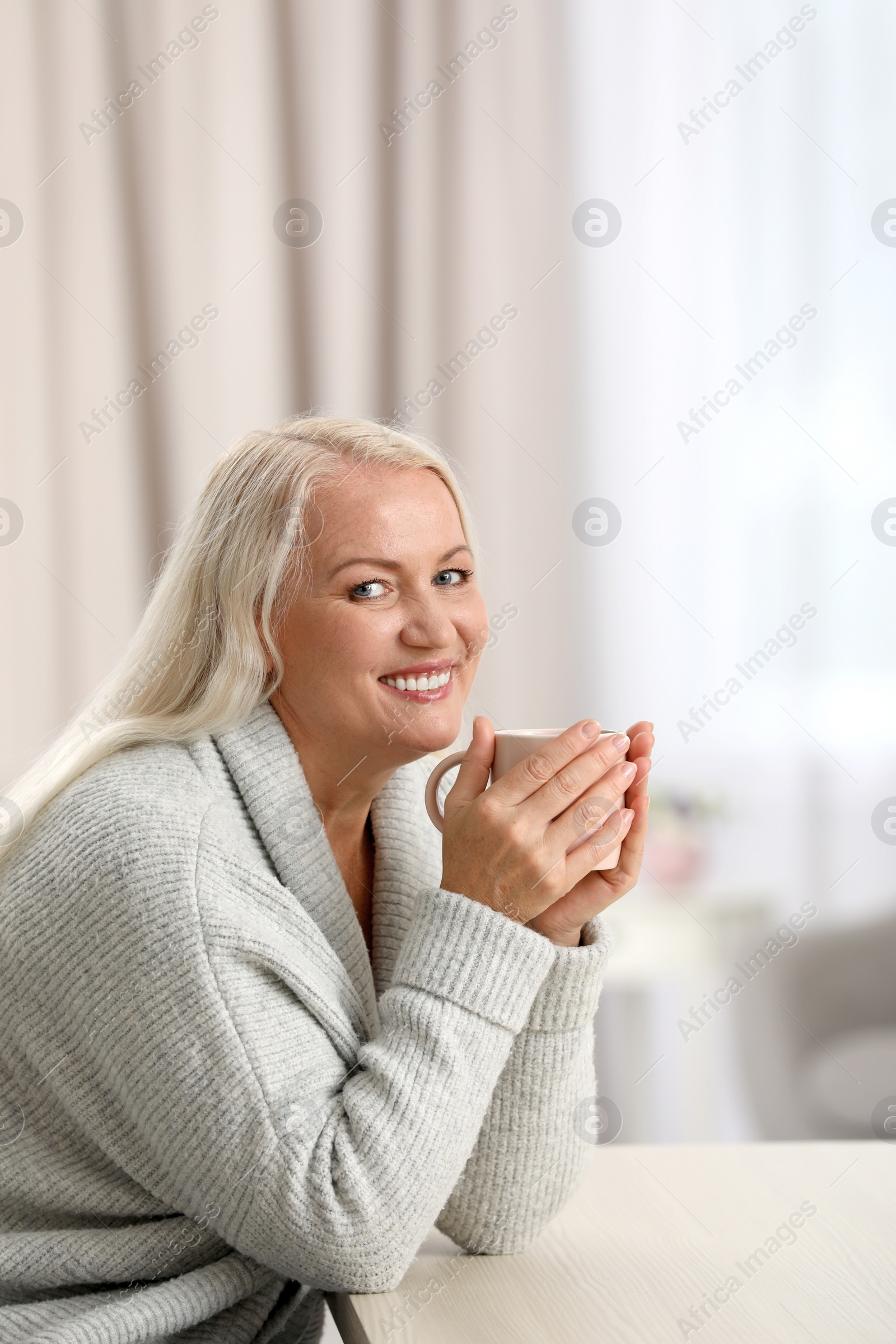Photo of Portrait of beautiful older woman with cup of tea sitting at table indoors