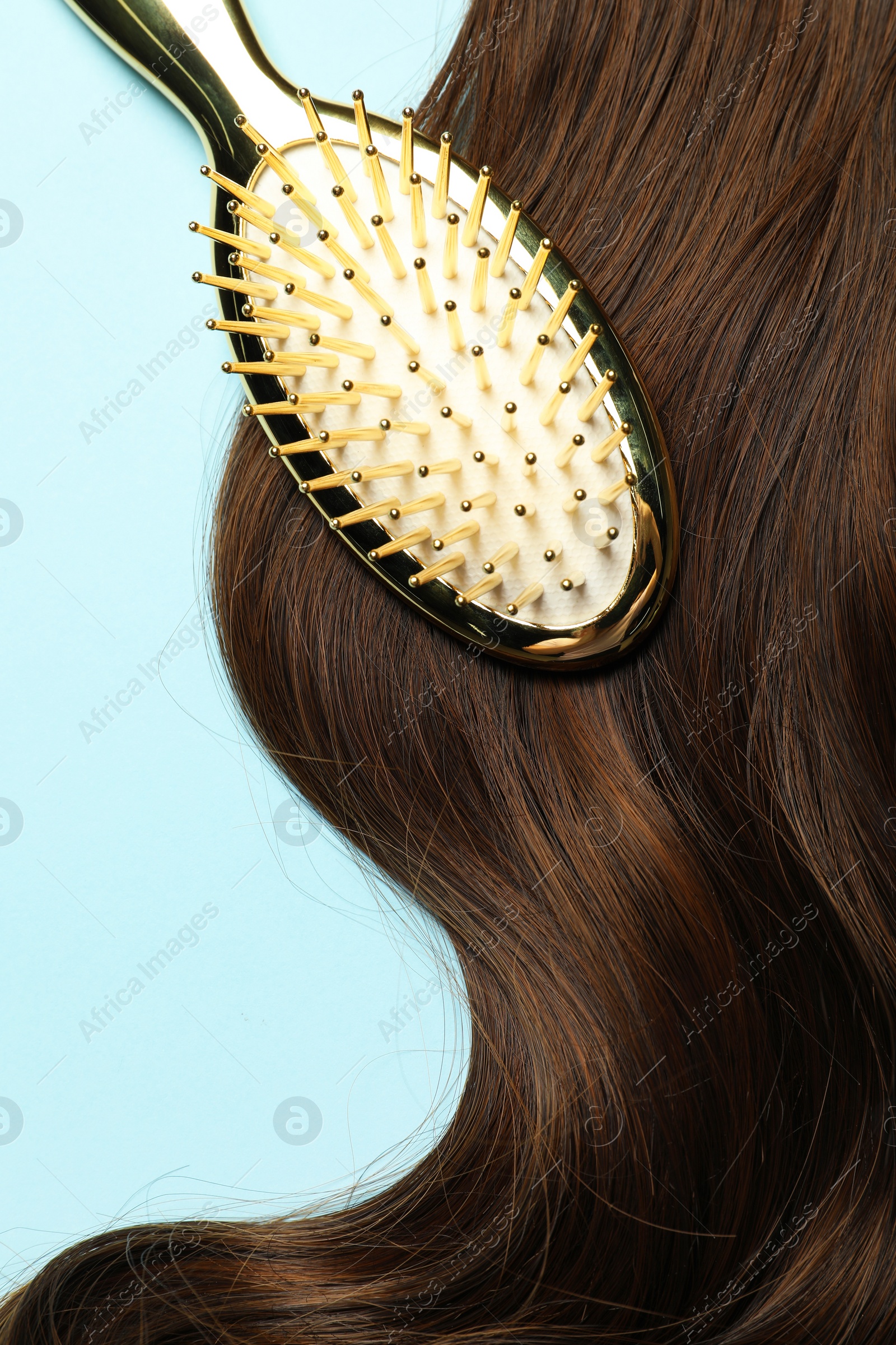 Photo of Stylish brush with brown hair strand on light blue background, top view