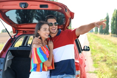 Happy young couple standing near car in shade
