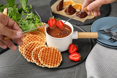 Photo of People dipping strawberries into fondue pot with milk chocolate at table, closeup