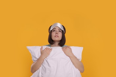Unhappy young woman with sleep mask and pillow on yellow background. Insomnia problem