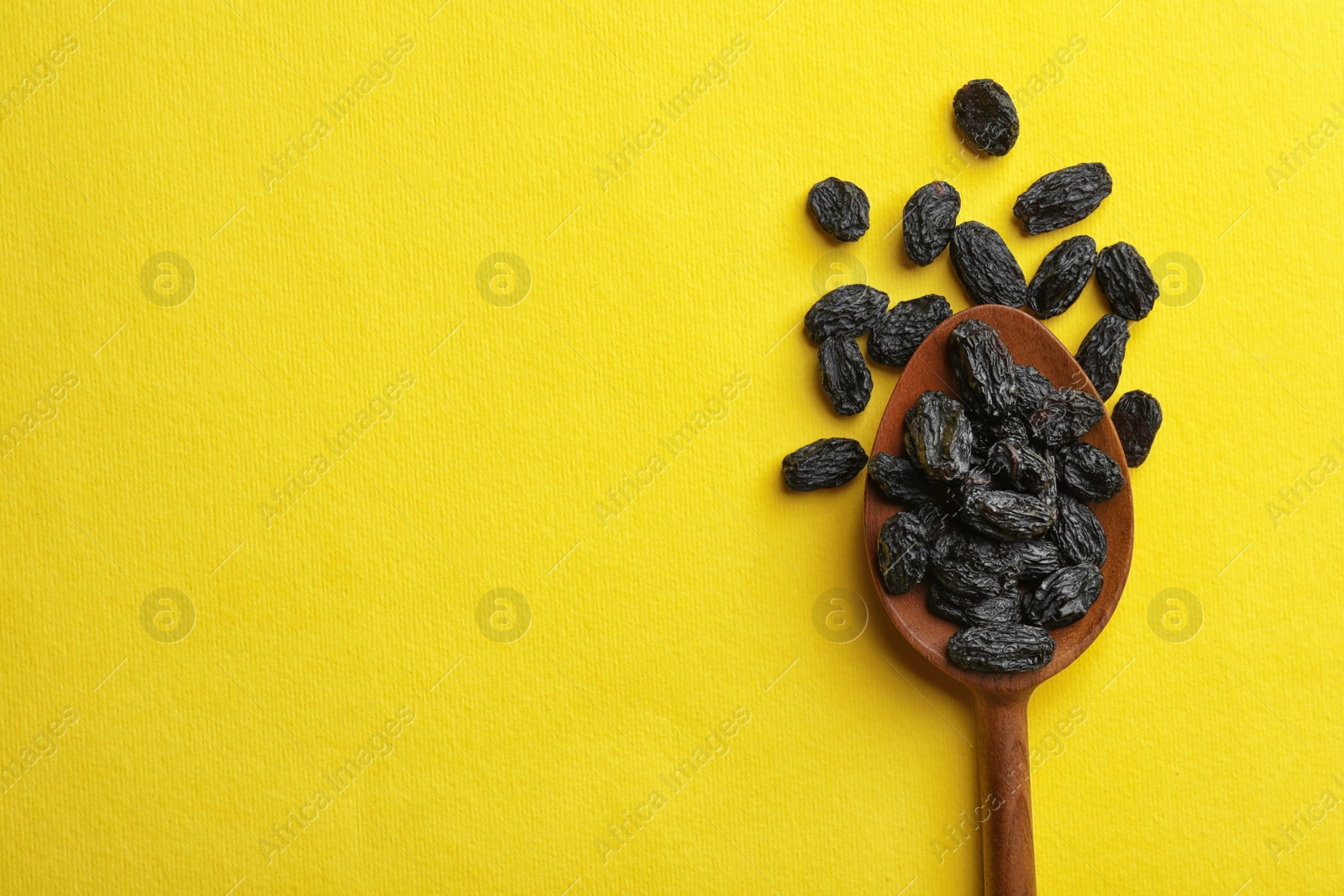 Photo of Spoon with raisins and space for text on color background, top view. Dried fruit as healthy snack