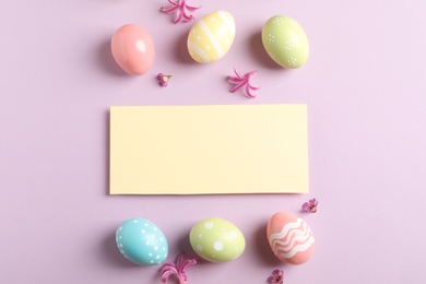 Flat lay composition with painted Easter eggs and blank card on color background, space for text