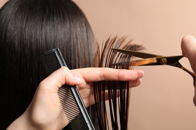 Photo of Hairdresser cutting client's hair with scissors on light brown background, closeup