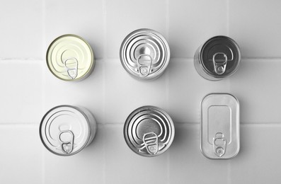 Photo of Many closed tin cans on white tiled table, flat lay