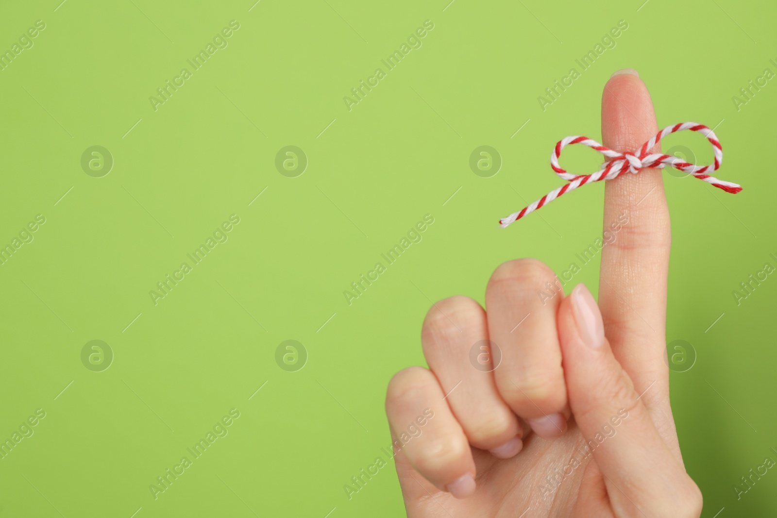 Photo of Woman showing index finger with tied bow as reminder on light green background, closeup. Space for text