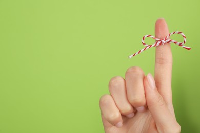 Photo of Woman showing index finger with tied bow as reminder on light green background, closeup. Space for text