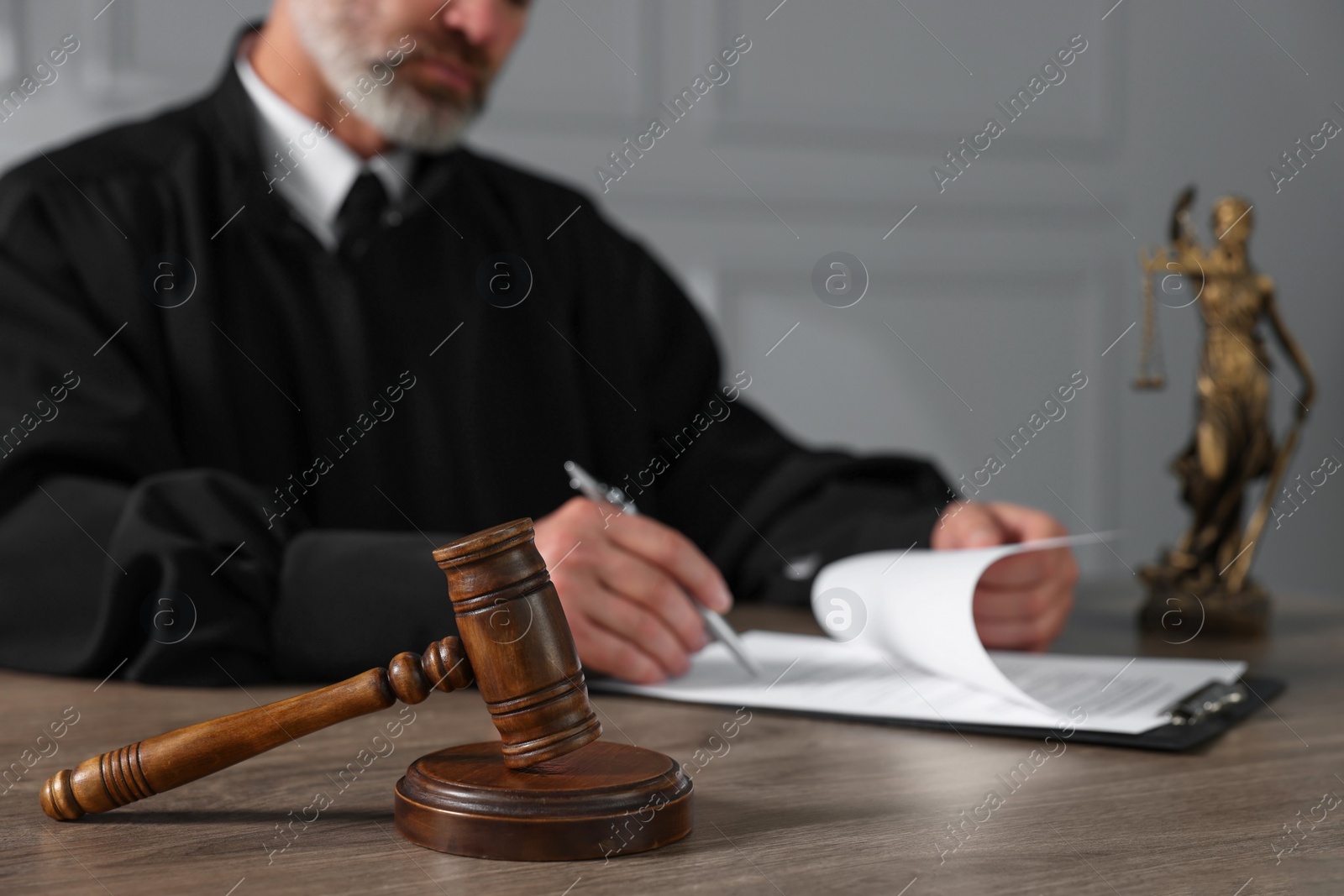 Photo of Judge with gavel writing in papers at wooden table indoors, closeup