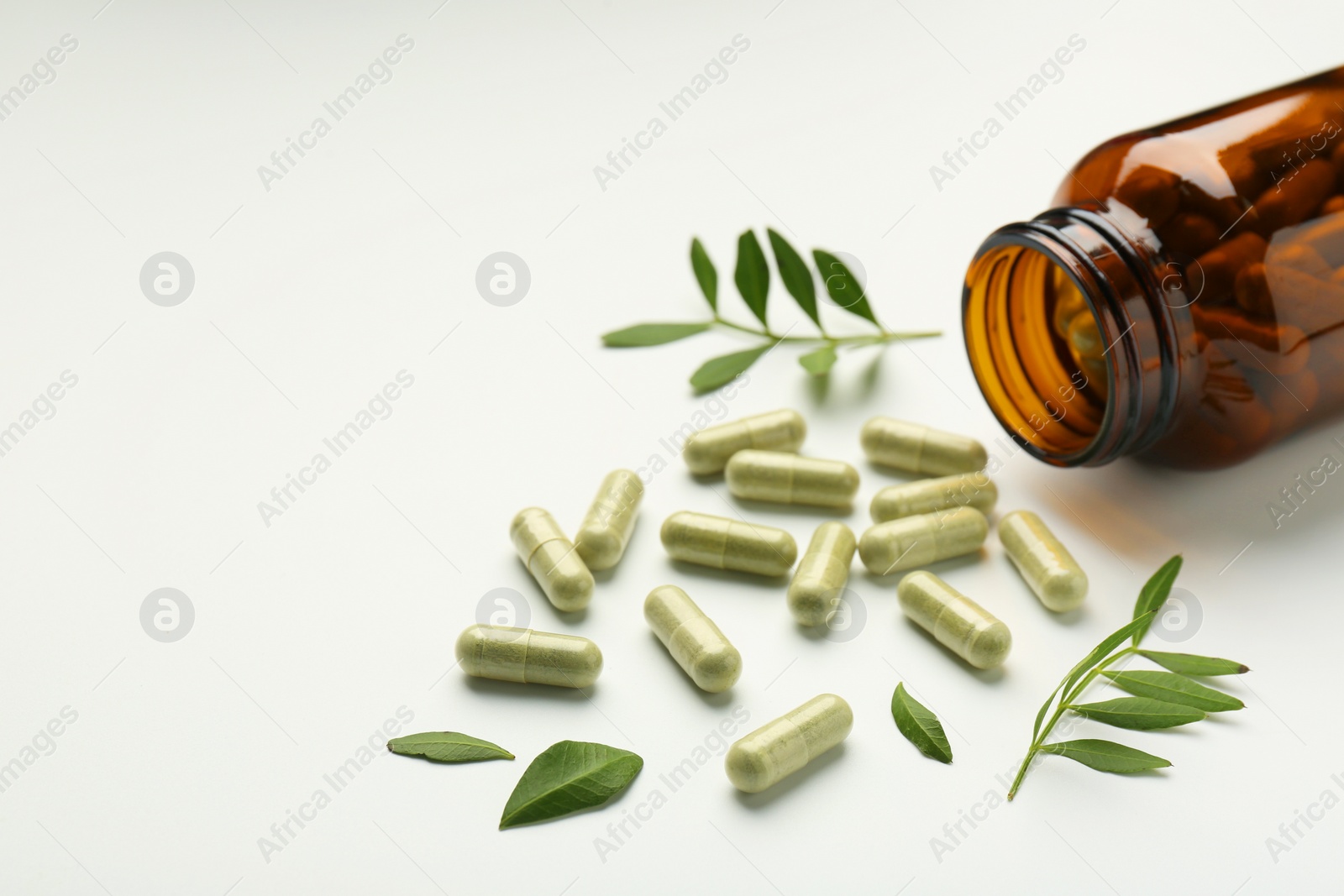 Photo of Bottle, vitamin capsules and leaves on white background, closeup. Space for text