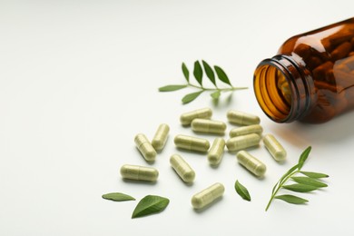 Bottle, vitamin capsules and leaves on white background, closeup. Space for text