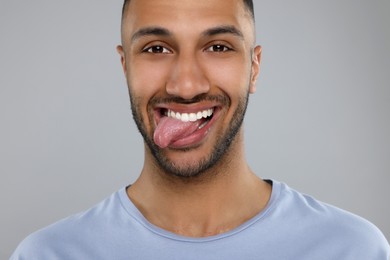 Photo of Happy young man showing his tongue on light grey background