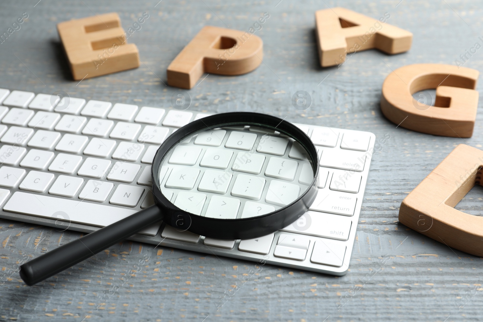 Photo of Magnifier glass, keyboard and letters on light grey wooden table, closeup. Find keywords concept